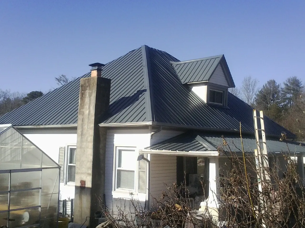 Dark blue standing seam metal roof on a white farmhouse with dormer — Slate & Tile Roof Repair by Roofing Brothers in North Grafton