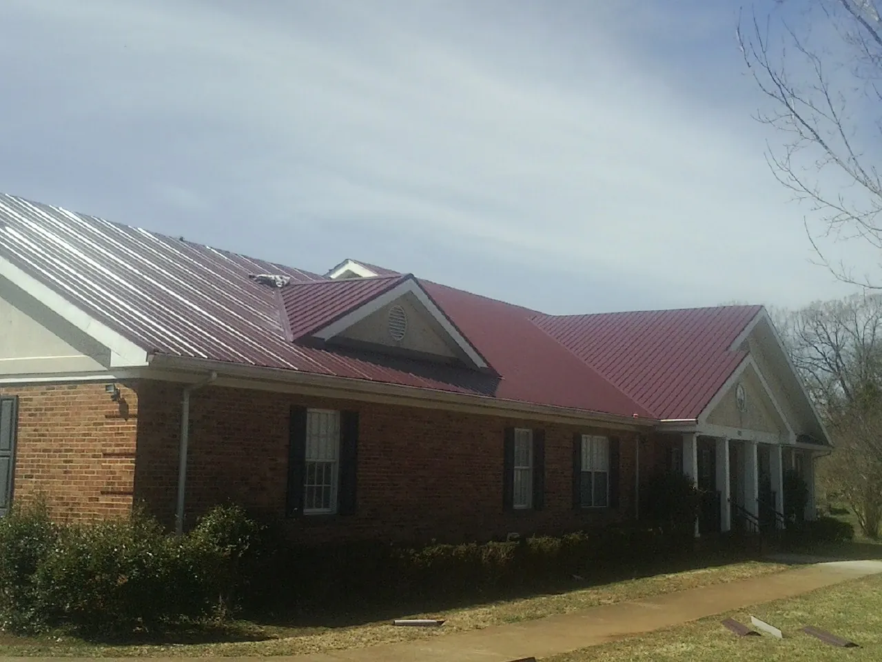 Red metal roof with gabled entries on a long brick building, from a Hail Damage Roof Repair job in North Grafton