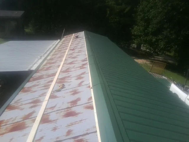 Old rusted panels beside newly installed green metal roofing — Wind Damage Roof Repair by Roofing Brothers in North Grafton