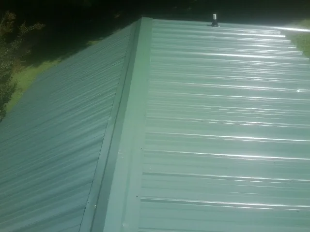 New green metal panels meeting at the ridge of a roof — Flat Roof Repair work by our crew in North Grafton
