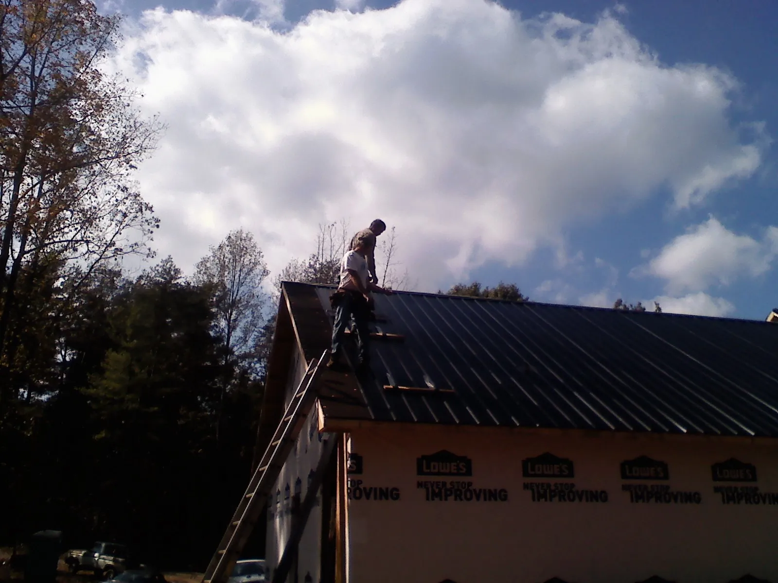 Roofer fastening dark metal panels high against a cloudy sky, from a Roof Inspection job in North Grafton