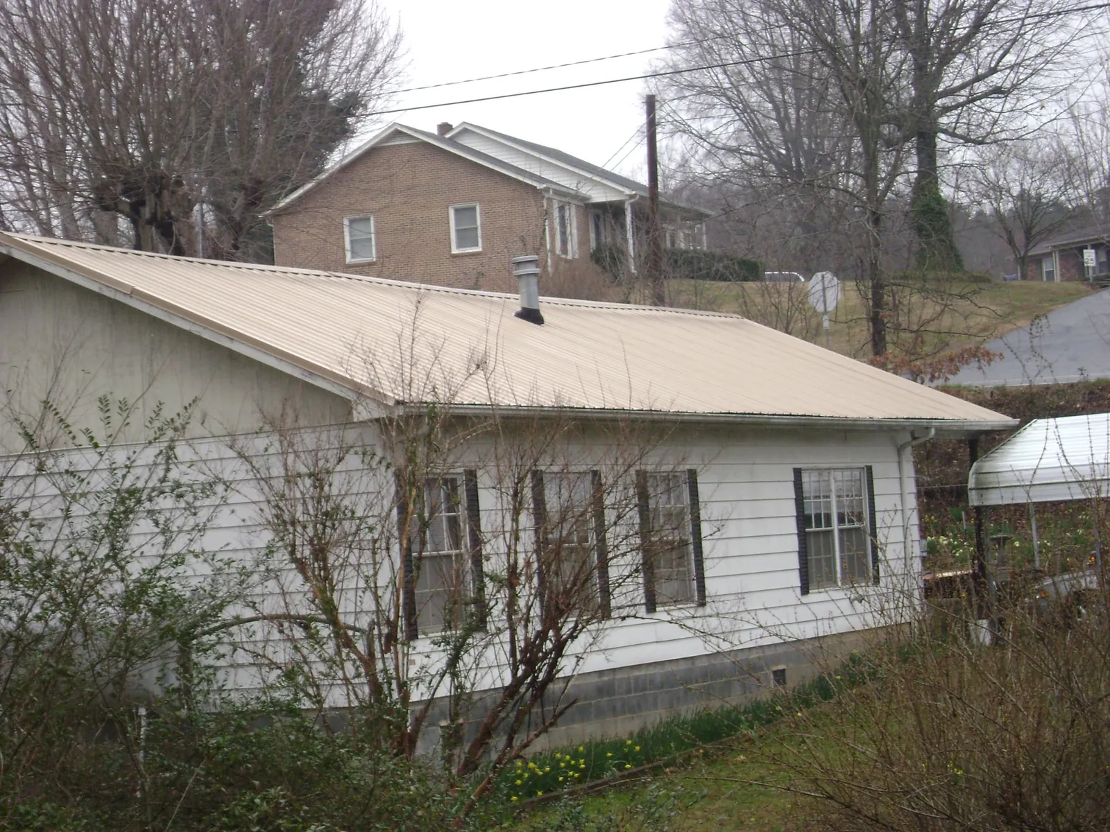 Tan metal roof on a white sided house set into a hillside — Commercial Roofing by Roofing Brothers in North Grafton