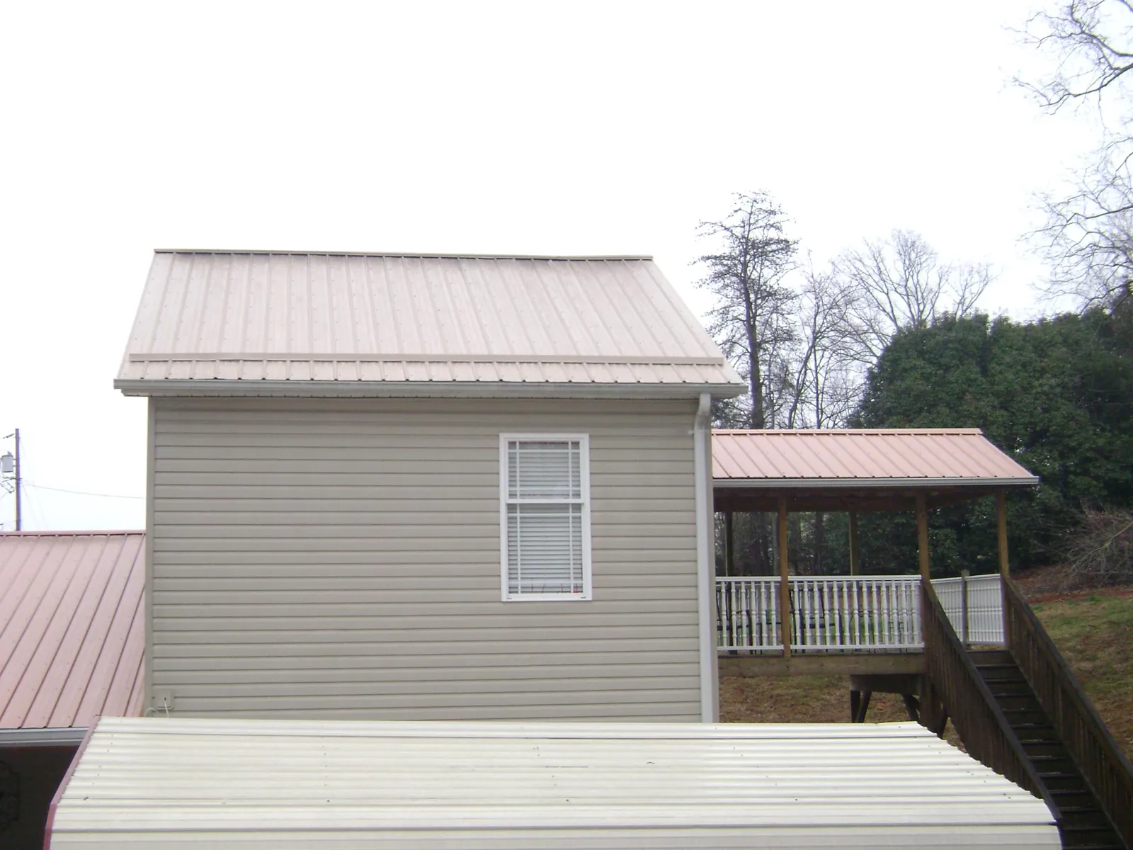 Tan metal roofs on a two story addition and attached porch, from a Roof Replacement job in North Grafton